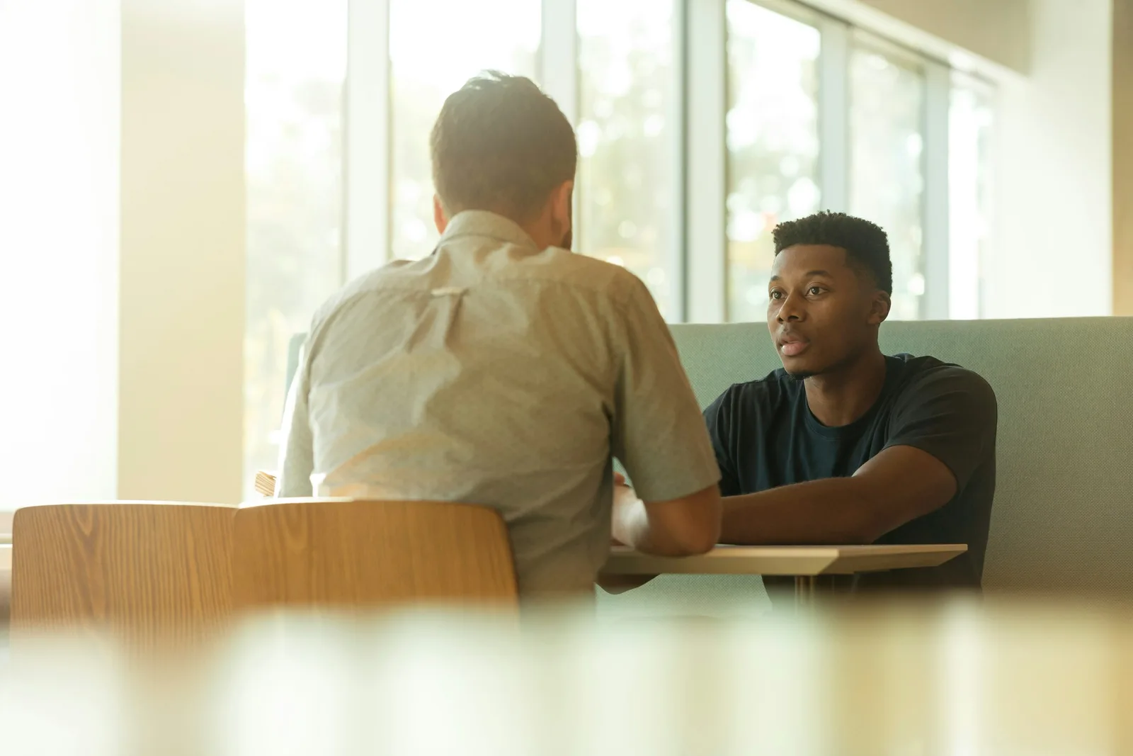Two colleagues sitting across a table in conversation, one listening closely as the other speaks