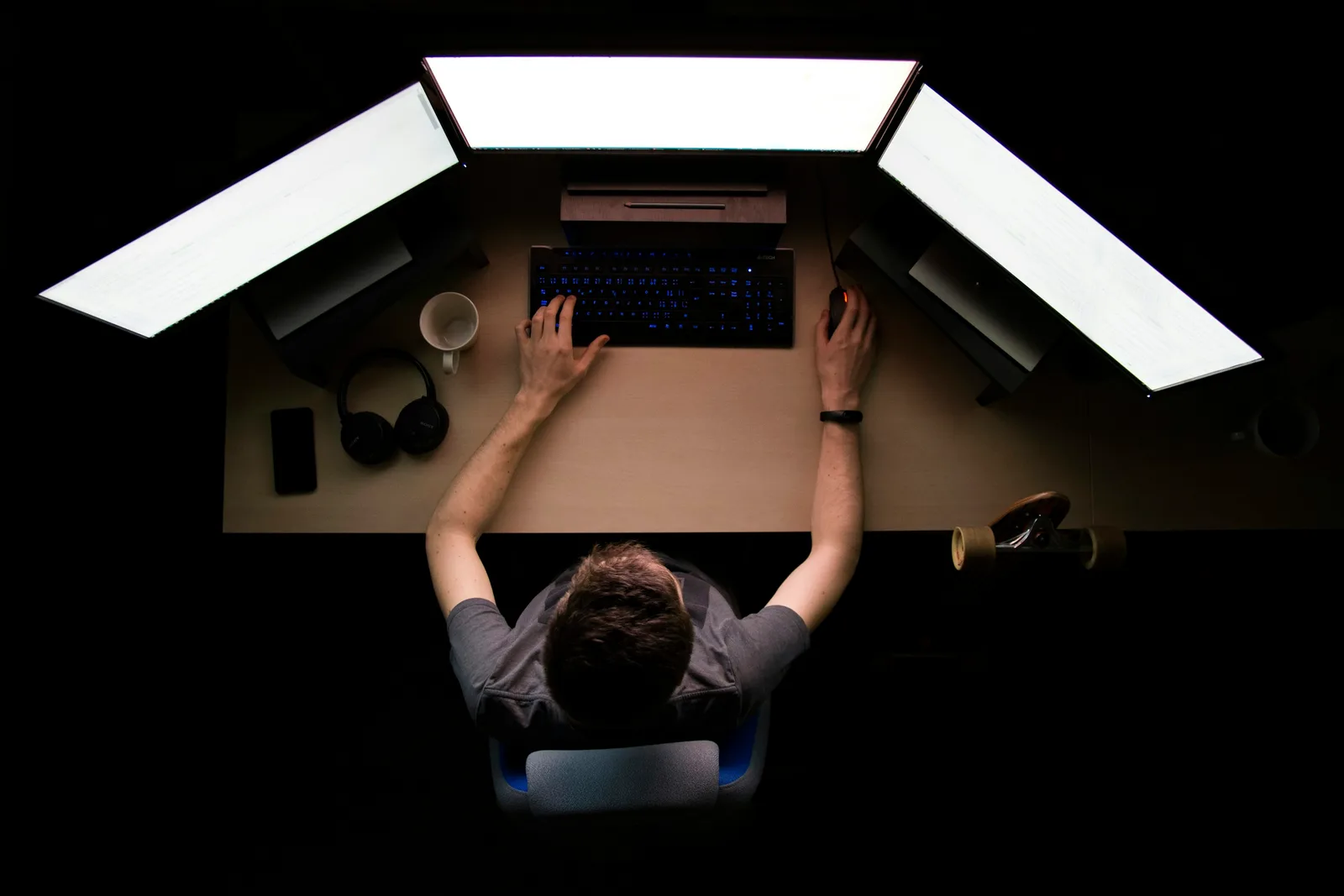 A person working alone at a laptop late at night, lit only by the glow of the screen