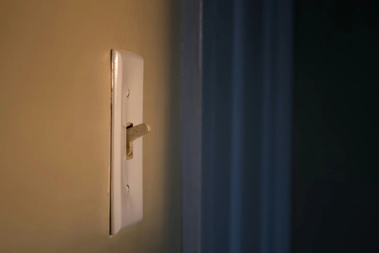 A light switch on a warm lit wall beside a doorway falling into shadow