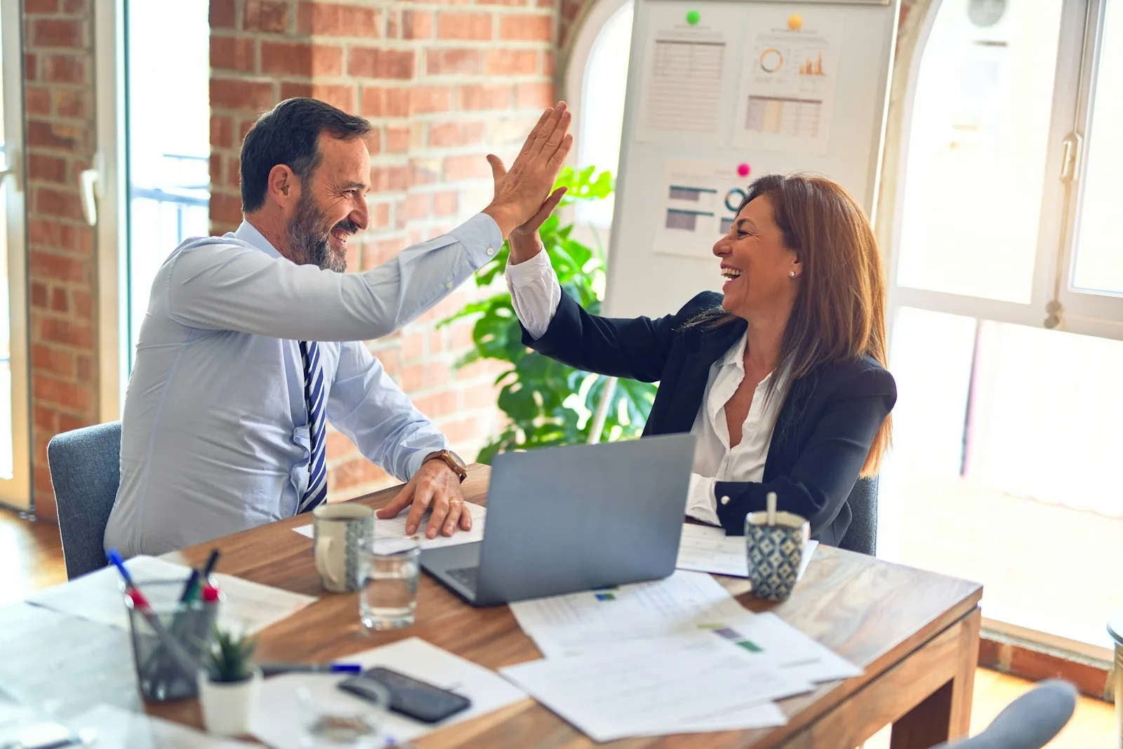 Two colleagues high-fiving across a desk in an office